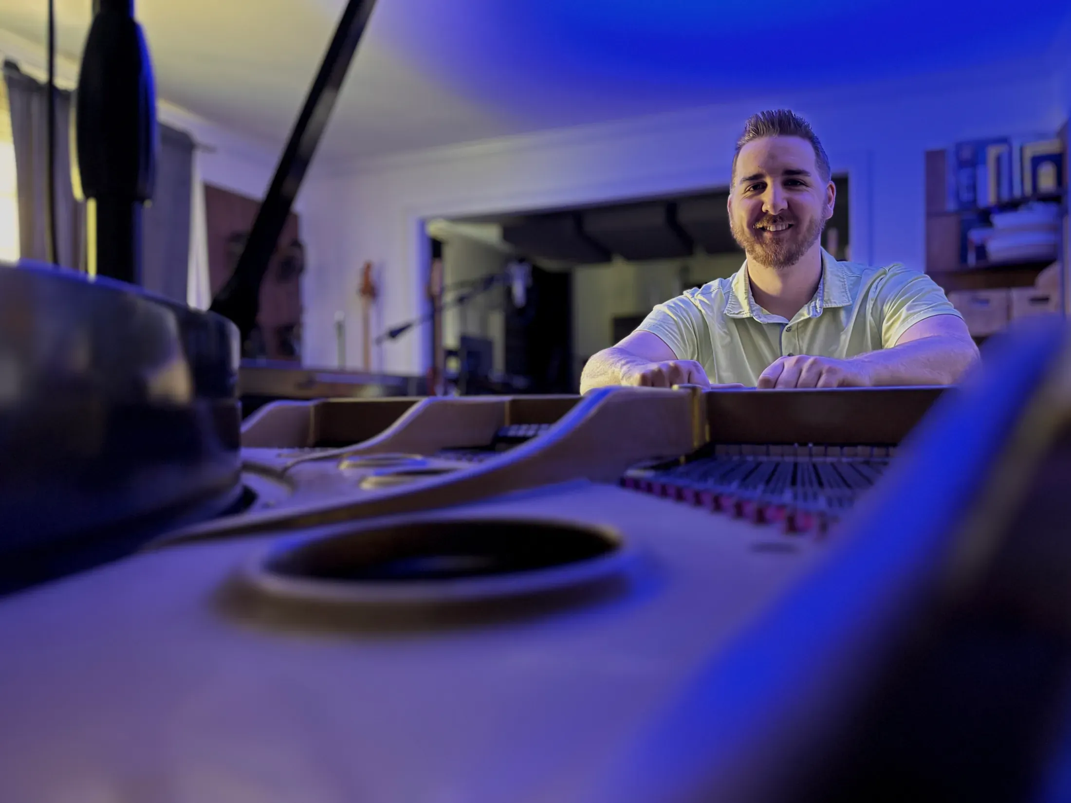 Pierce O’Brien behind an open grand piano in a blue-lit studio