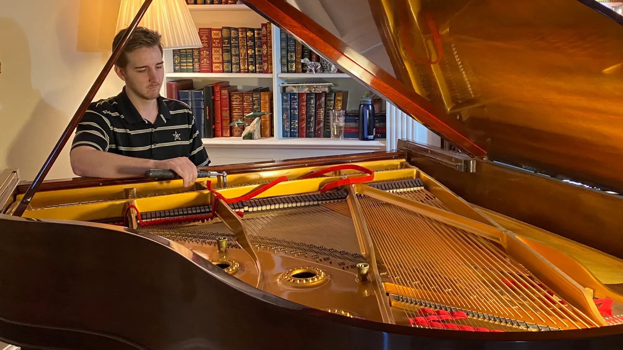 Pierce O’Brien tuning a grand piano in a room lined with books